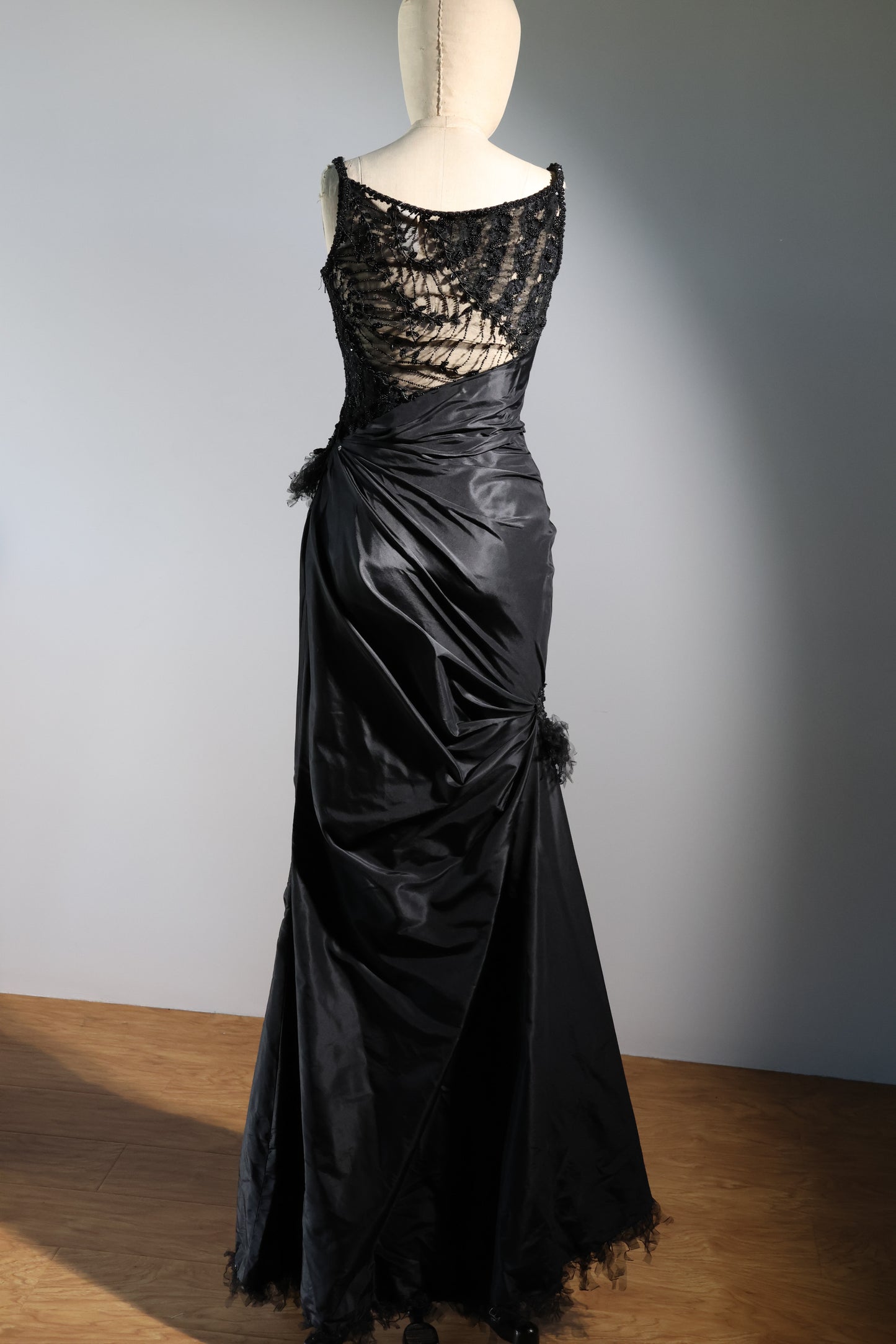 Black evening gown with lace detailing on a mannequin against a plain background