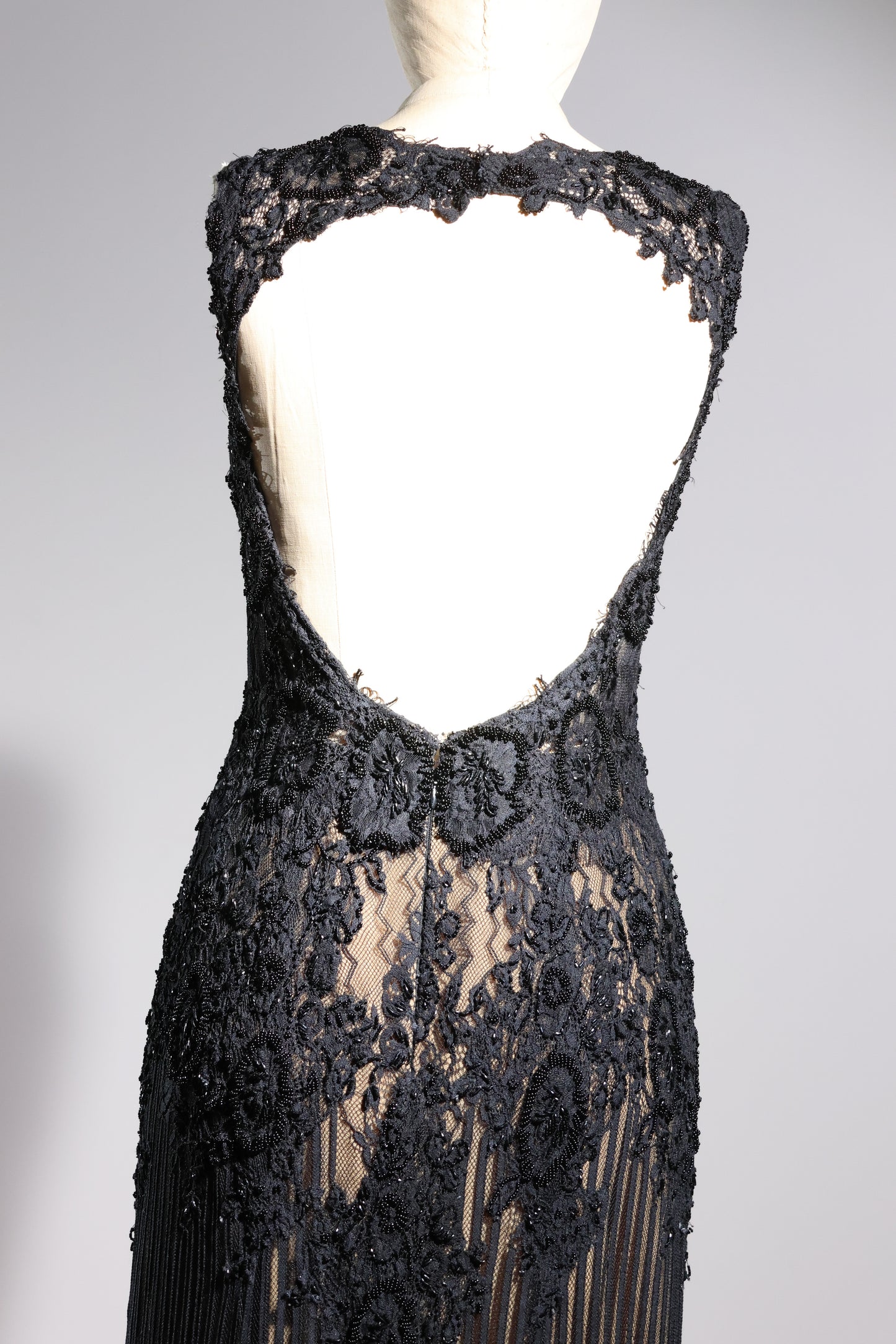 Black lace evening gown on a mannequin against a gray background