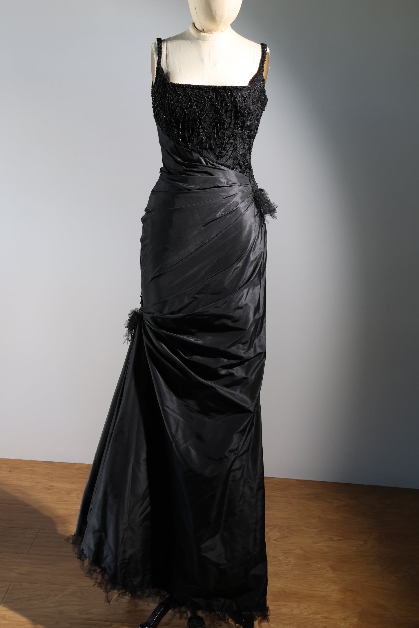 Black evening gown on a mannequin against a plain background