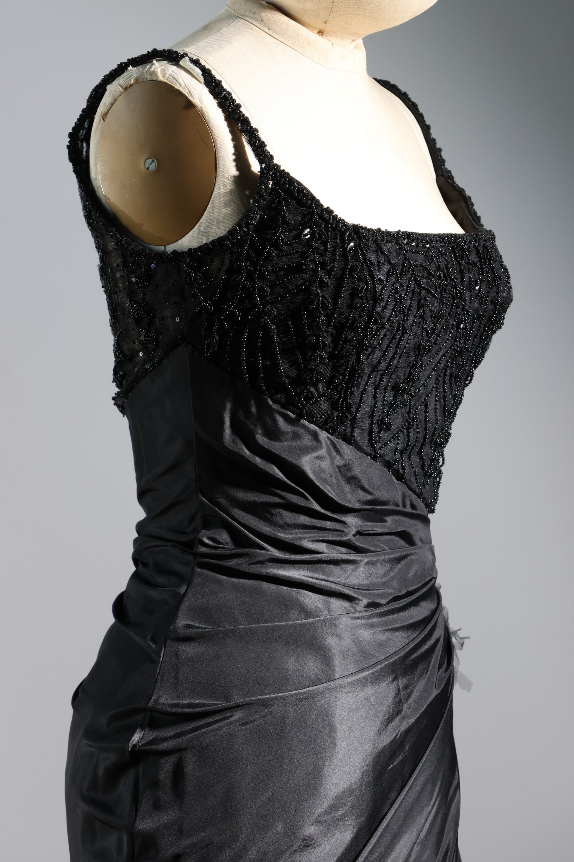 Black evening gown with intricate detailing on a mannequin against a gray background