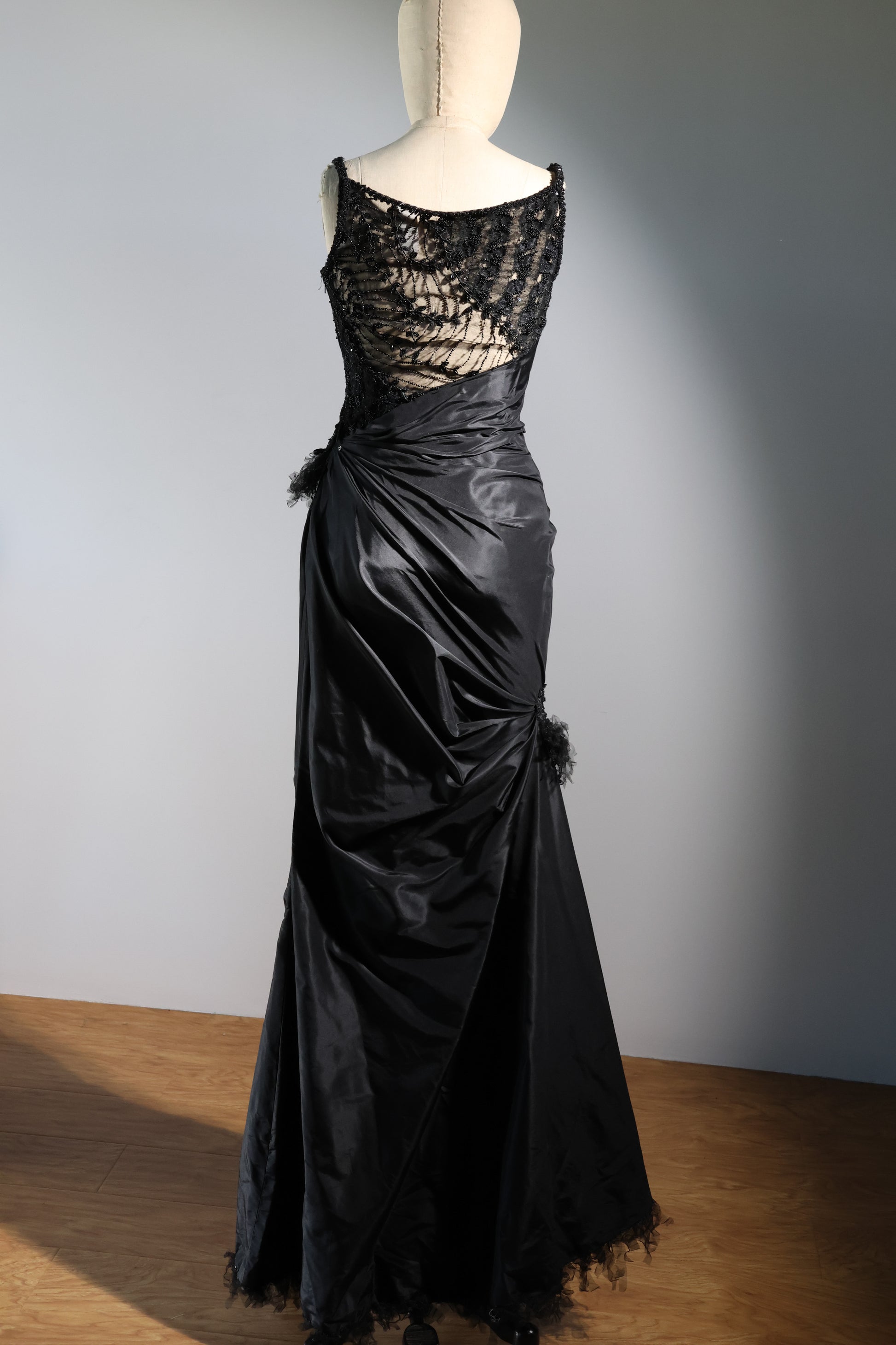 Black evening gown with lace detailing on a mannequin against a plain background